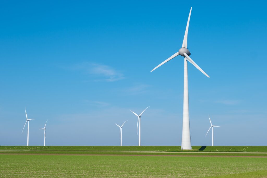 A group of wind turbines gracefully spin in a vast green field, harnessing the power of the wind to